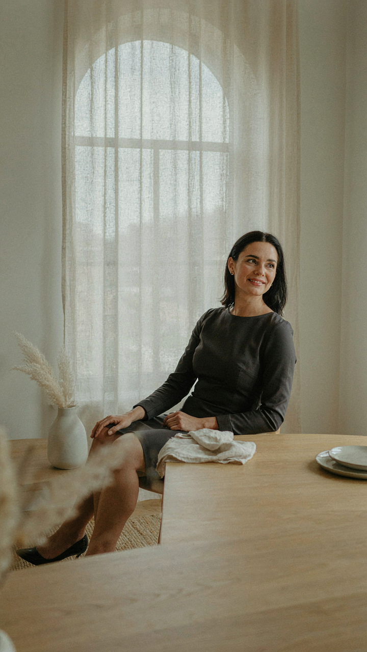 A woman in a tailored dress sits comfortably at a fine dining table.