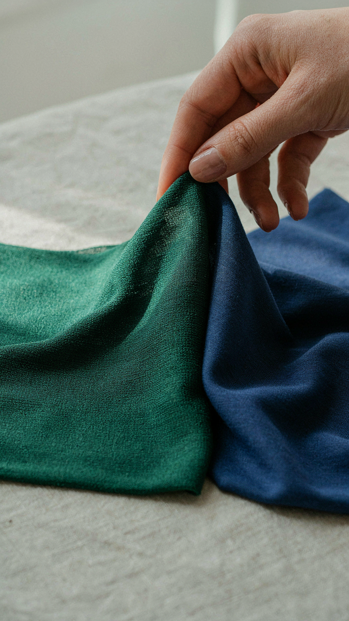 A hand touches two fabric swatches, showing different textures and drapes.