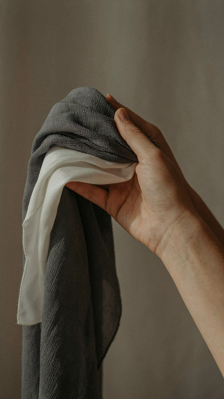 A hand holds swatches of dense crepe and crisp silk blend fabrics.