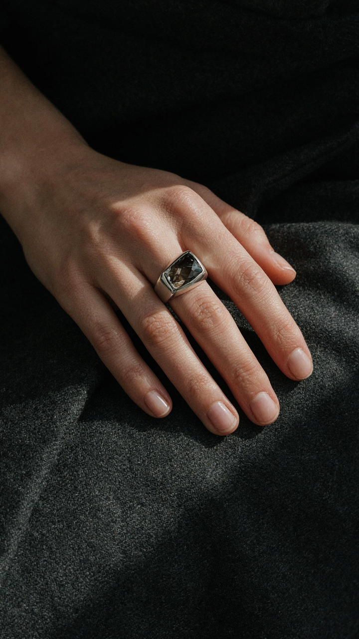 A hand with a large cocktail ring rests on a dark wool wrap.