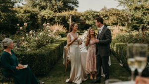 Wedding guests in elegant fascinators chat at an outdoor reception.