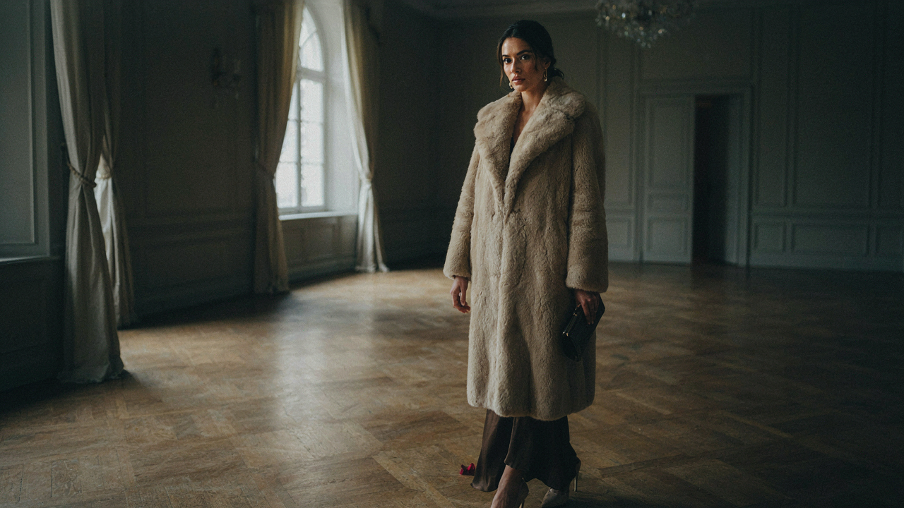 A woman in a champagne faux fur coat in an elegant ballroom exudes confidence.