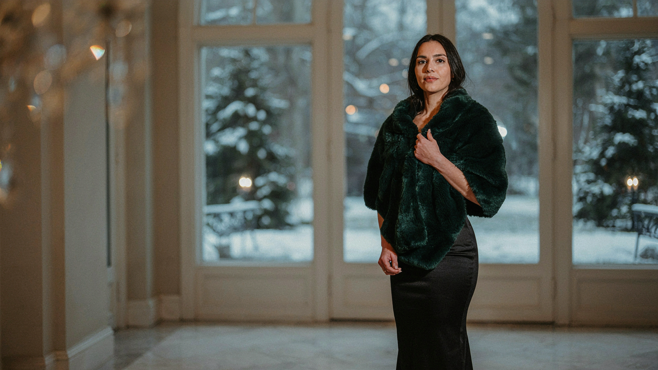 Woman wearing an elegant emerald faux fur wrap evening stole over a black gown.