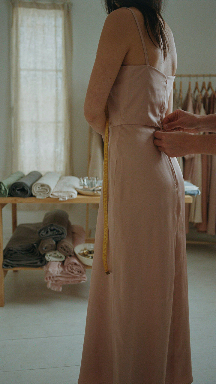 A tailor's hands adjusting the waist seam of a dress on a client.