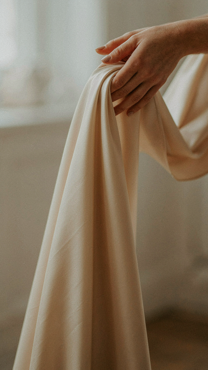 A hand gently drops a piece of smooth, flowing silk fabric.