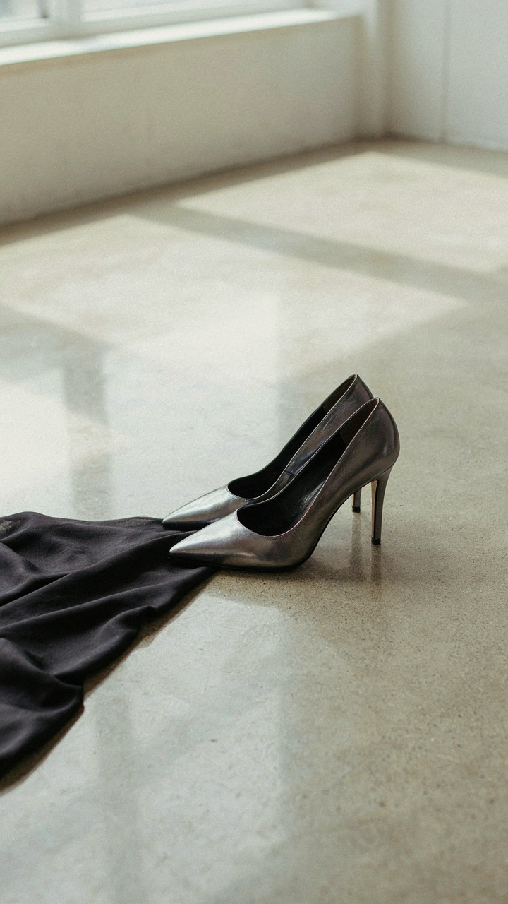 Elegant, architectural heels with a metallic finish next to flowing dark fabric.