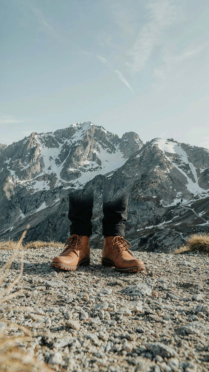 Feet in elegant, low-heeled boots with textured soles stand on gravel.