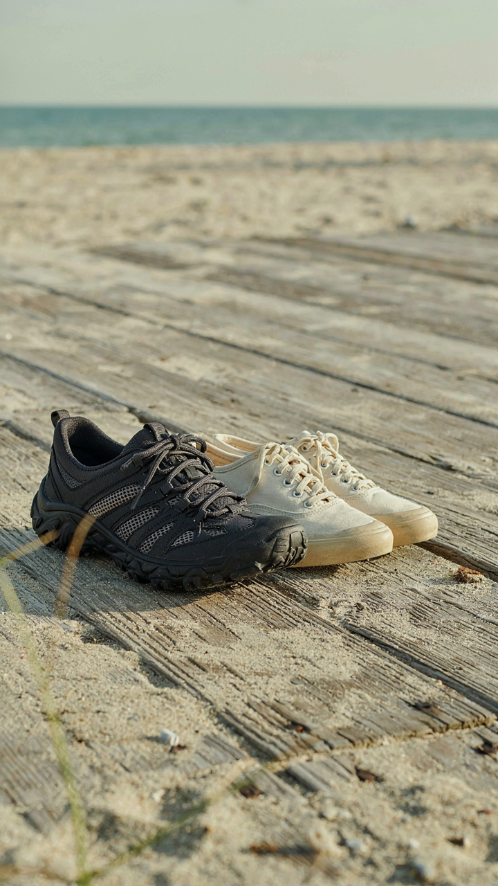 Water shoes and canvas sneakers sit on a sandy boardwalk.