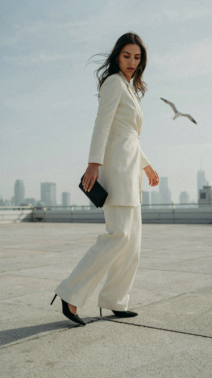 A woman in a jumpsuit stumbles on a windy rooftop, her heel caught in a gap.