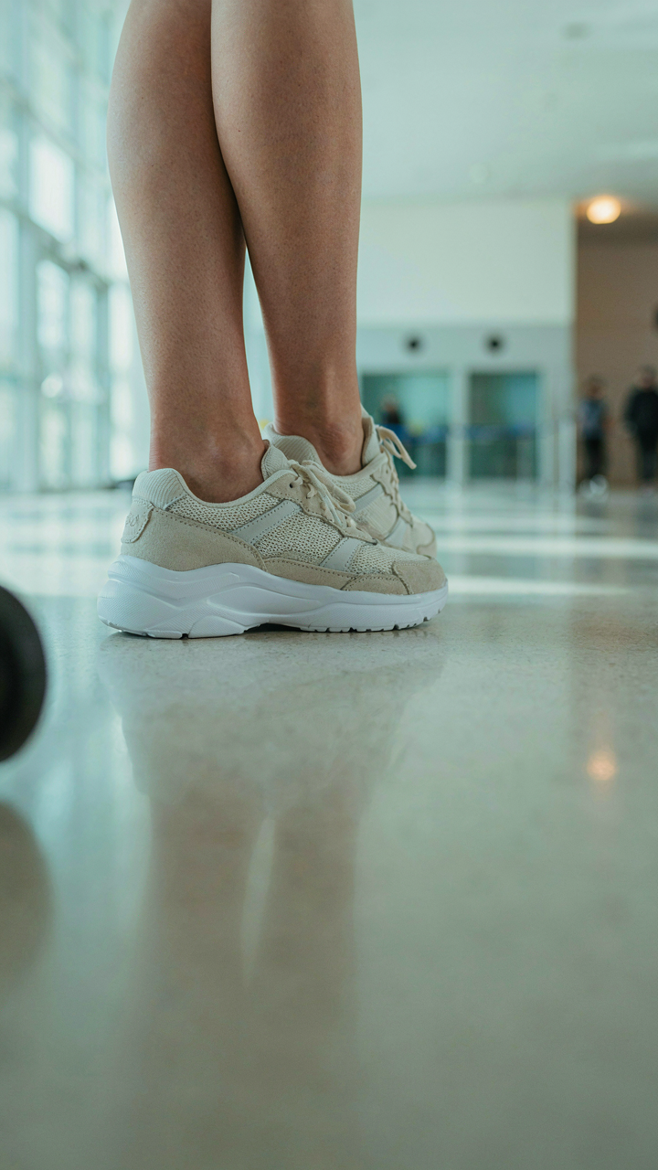 Close-up of supportive sneakers on a woman's feet, standing on a shiny airport floor.