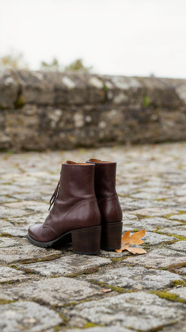Elegant dark leather ankle boots with sturdy heels stand on cobblestones.