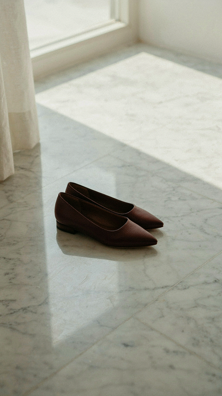 Sleek, pointed-toe flats rest on a polished marble floor.