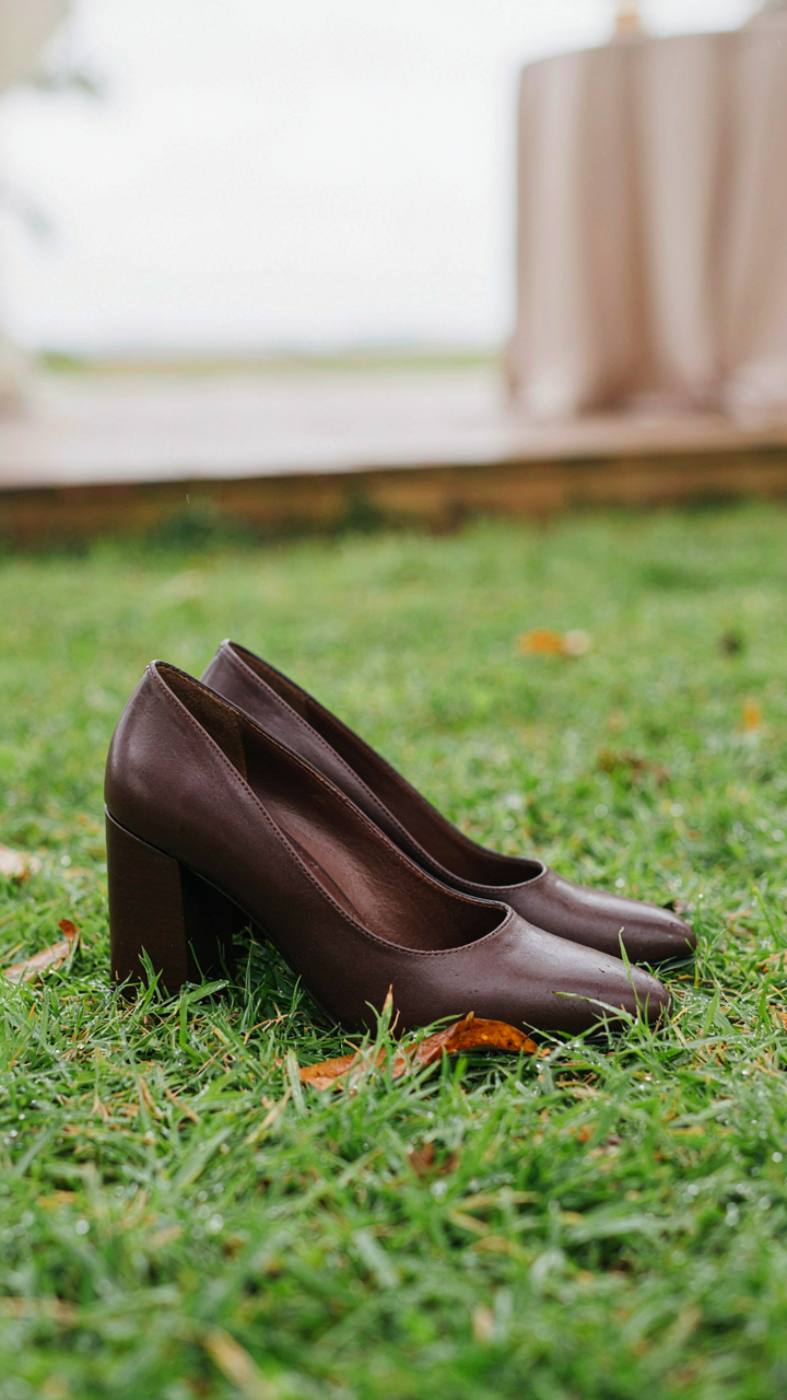Dark brown leather closed-toe block heels on damp green grass.