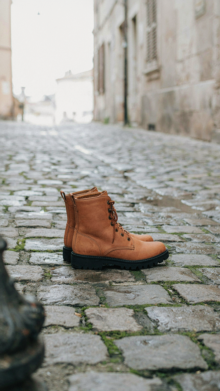 Waterproof leather boots with thick rubber soles stand on an uneven cobblestone street.