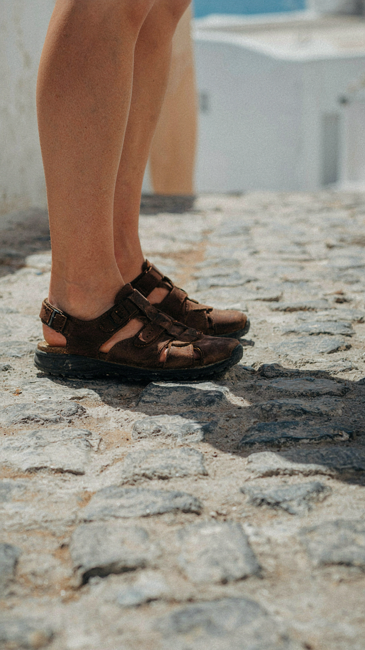 Person's feet in sturdy sandals with rubber soles walking on old cobblestones.