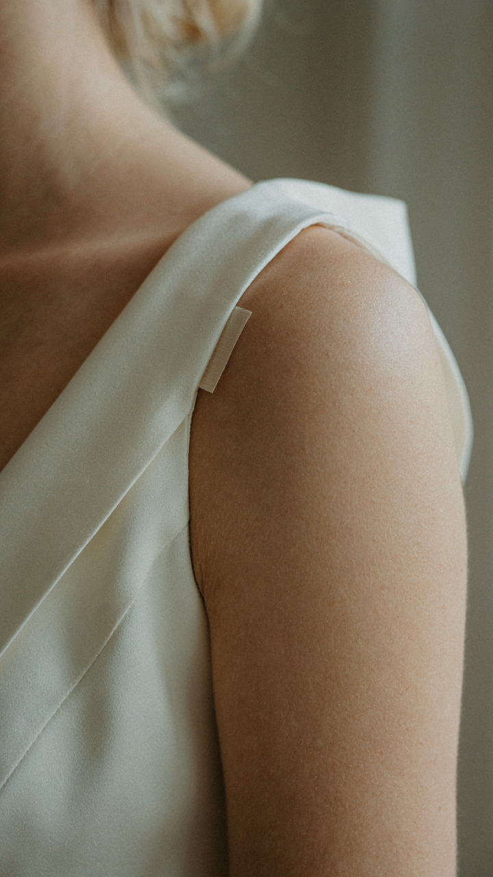Fashion tape secures a silk shawl to a wedding guest dress on a woman's shoulder.