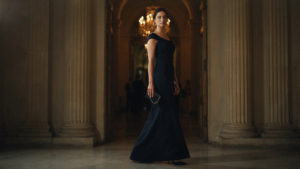 An elegant woman in a navy gown enters a softly lit ballroom for a fundraiser dinner.
