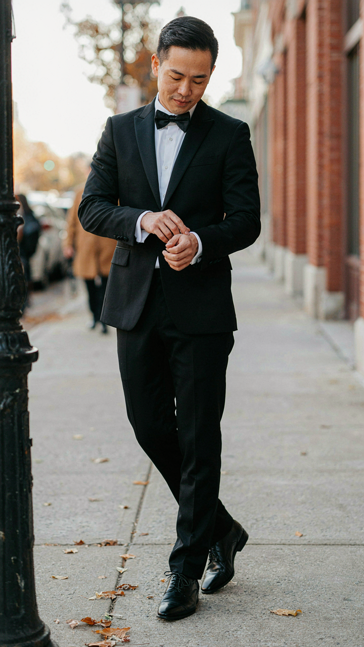 A person in a tuxedo pauses mid-step, casually adjusting their cuff.