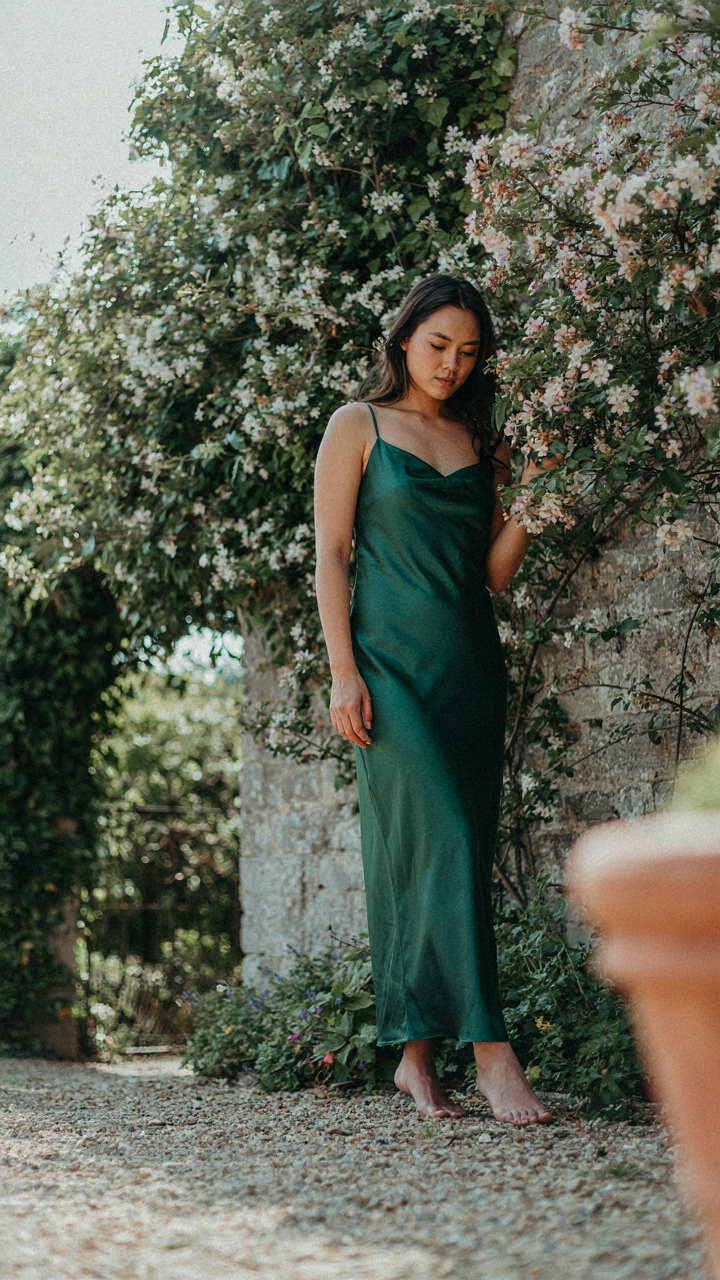 Woman in an elegant dress leans against an ivy-covered garden wall.