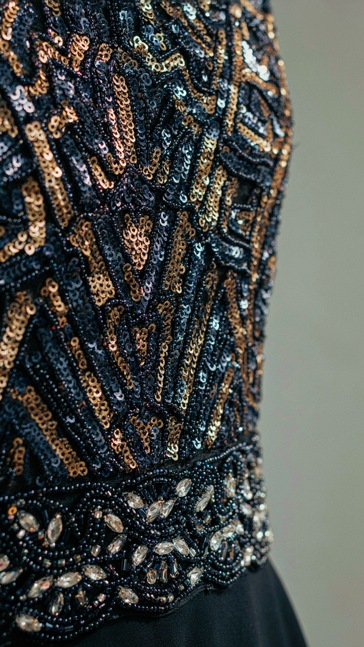 A close-up of an art deco sequined panel on a dark dress, catching light.