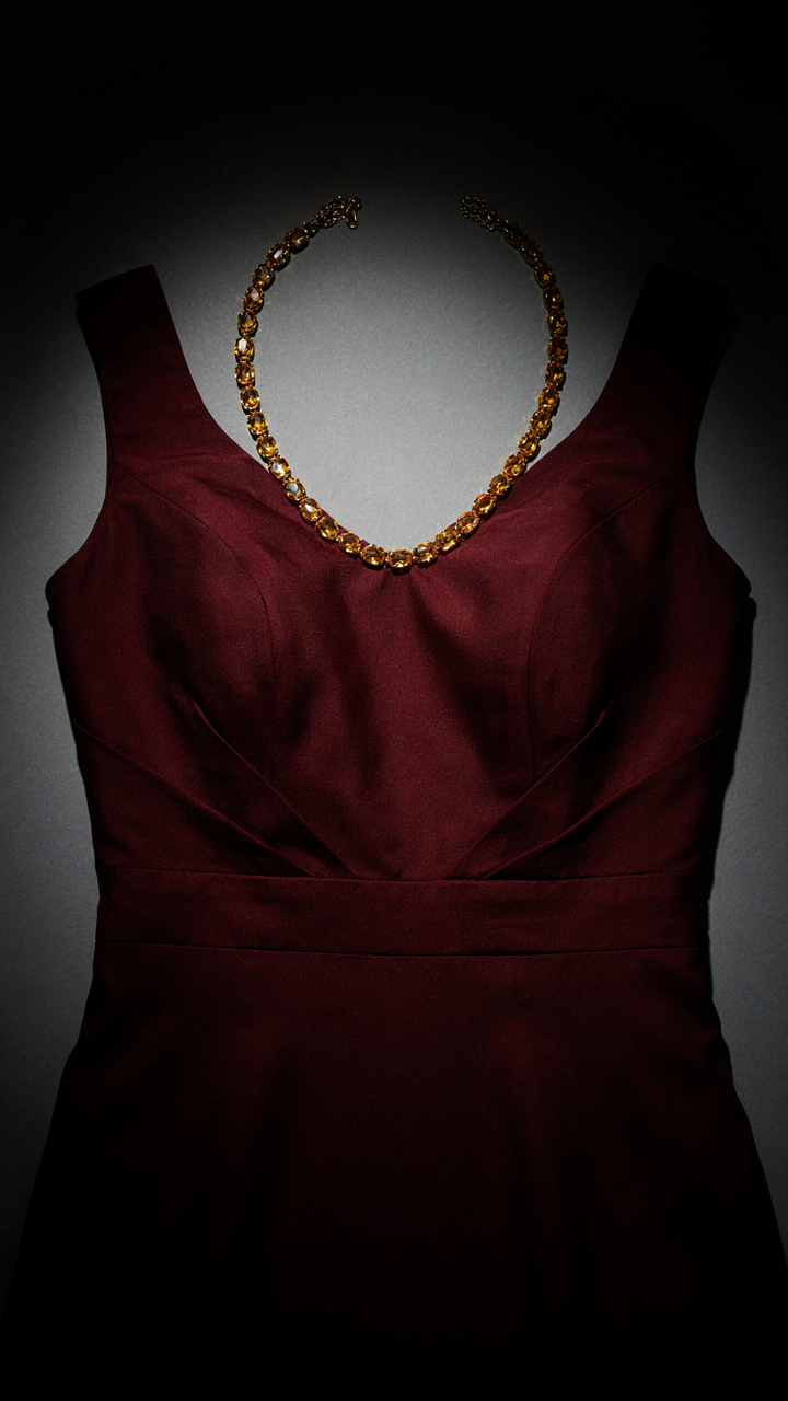 A warm citrine gemstone collar necklace rests on a burgundy cocktail dress.