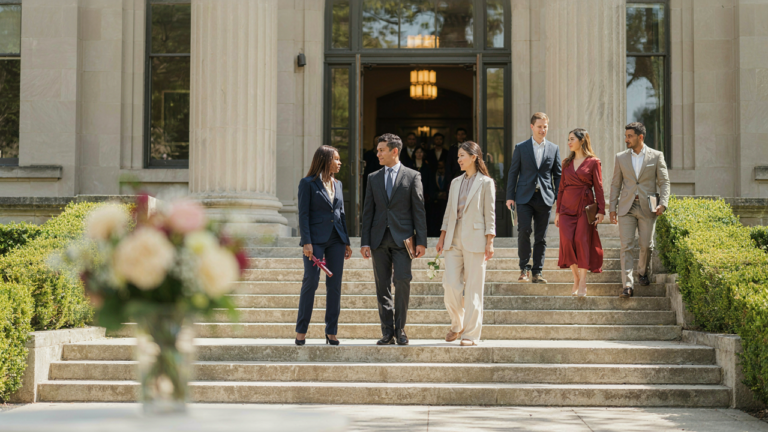 Adults in polished graduation ceremony guest outfits walk towards a building.