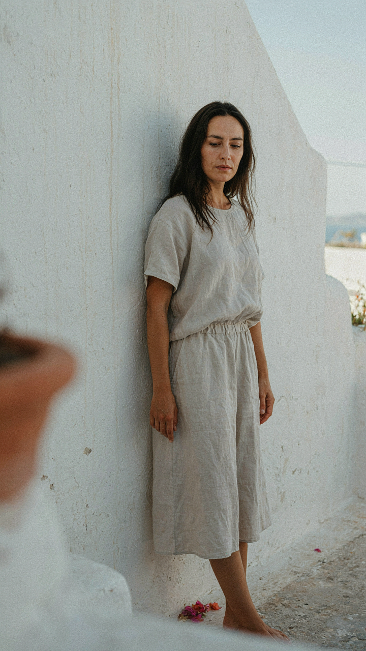 Woman in a light gray linen dress blending with a white wall in Santorini.