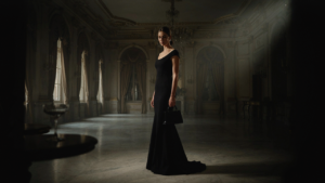 A woman in a black gown holds a small structured handbag in a ballroom.