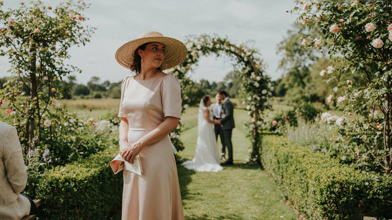 A woman in a stylish hat for wedding guest outfit, in a garden.