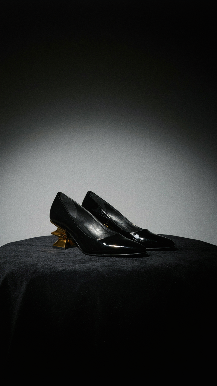 Formal black heels with an architectural gold-toned heel on dark fabric.