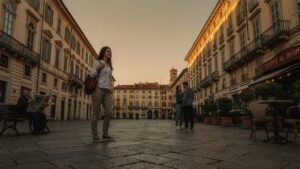 A woman stands in the middle of a large, old European town square at sunset, flanked by multi-story buildings with ornate facades and arched windows,