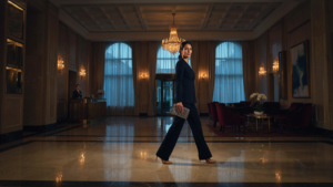 A woman in a navy jumpsuit walks through a grand hotel lobby, ready for a hotel wedding guest