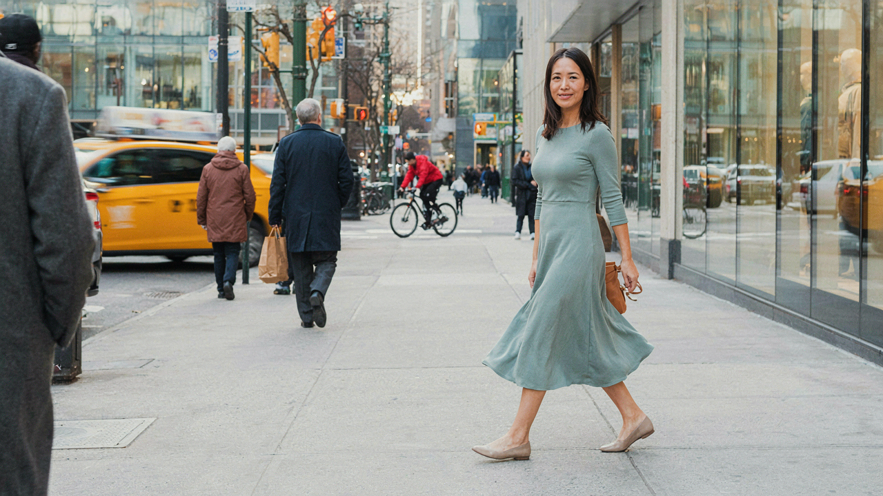 A woman confidently walking in a midi dress, looking back at the camera.