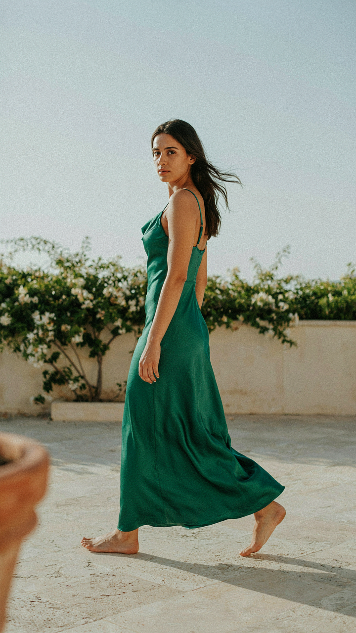 A woman in a satin dress, captured mid-stride with a subtle body twist.