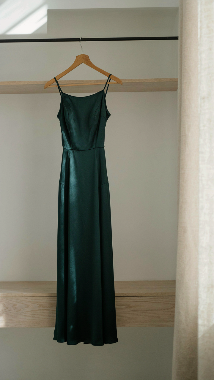 A single jewel-tone midi dress hanging in a minimalist closet.