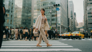 A traveler in a neutral outfit walks through a busy Tokyo street crossing.