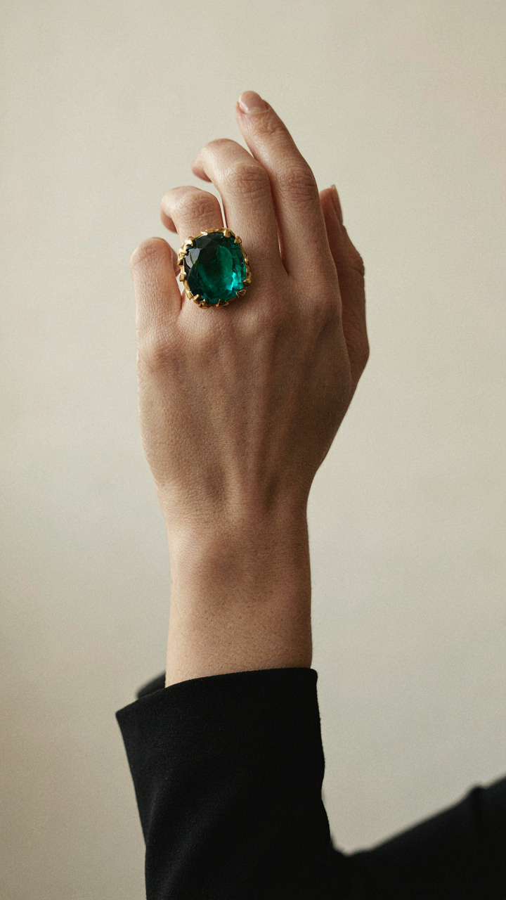A hand wearing a single dramatic cocktail ring with a black dress.