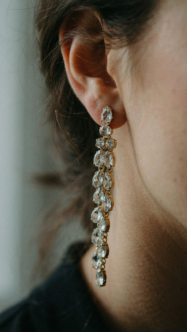 A woman wearing a long, moving chandelier earring with her black dress.