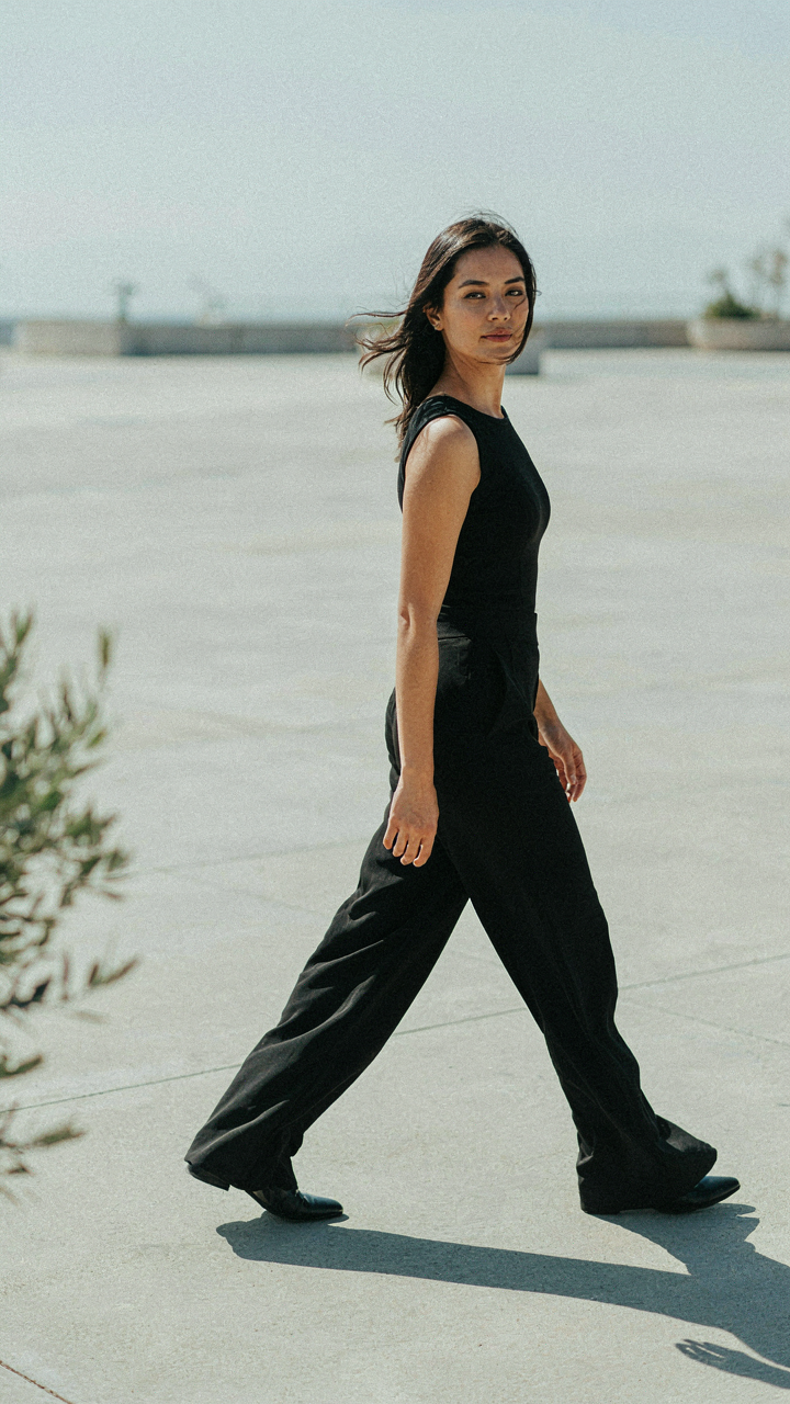 A woman in a wide-leg black jumpsuit walking gracefully.