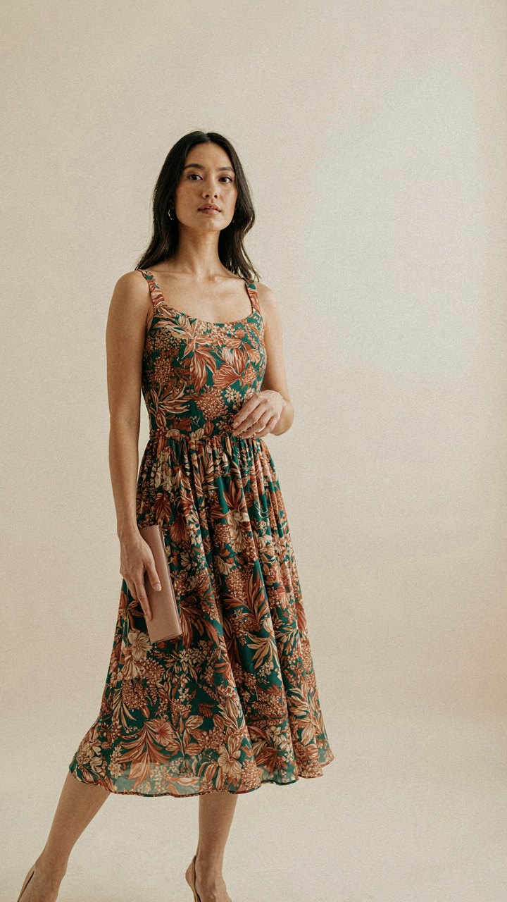 A woman in a flowy, patterned dress holds a thin, solid-colored clutch.