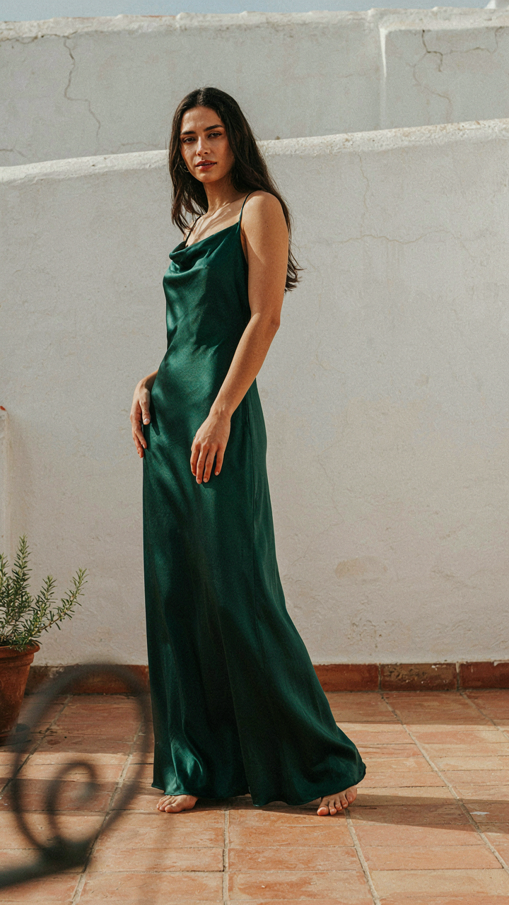 A woman in a long silk dress stands angled, allowing the fabric to drape gracefully.