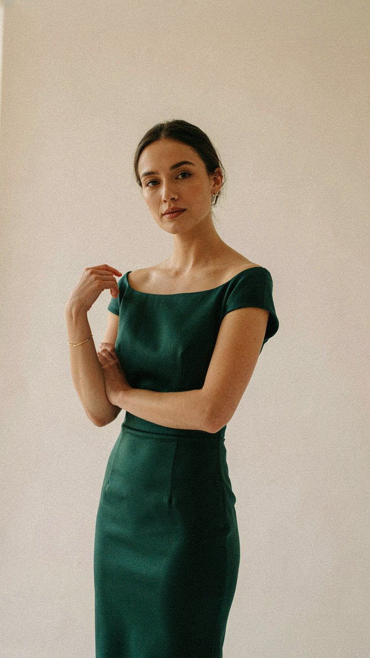 Woman in boat neck dress, with stud earrings, showing a simple bracelet.