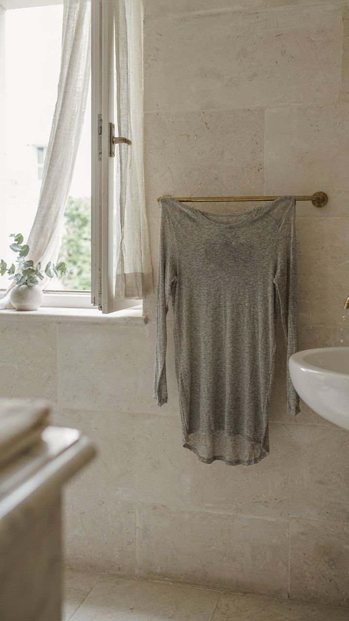 A damp merino wool shirt hangs drying on a towel rack in a hotel bathroom.