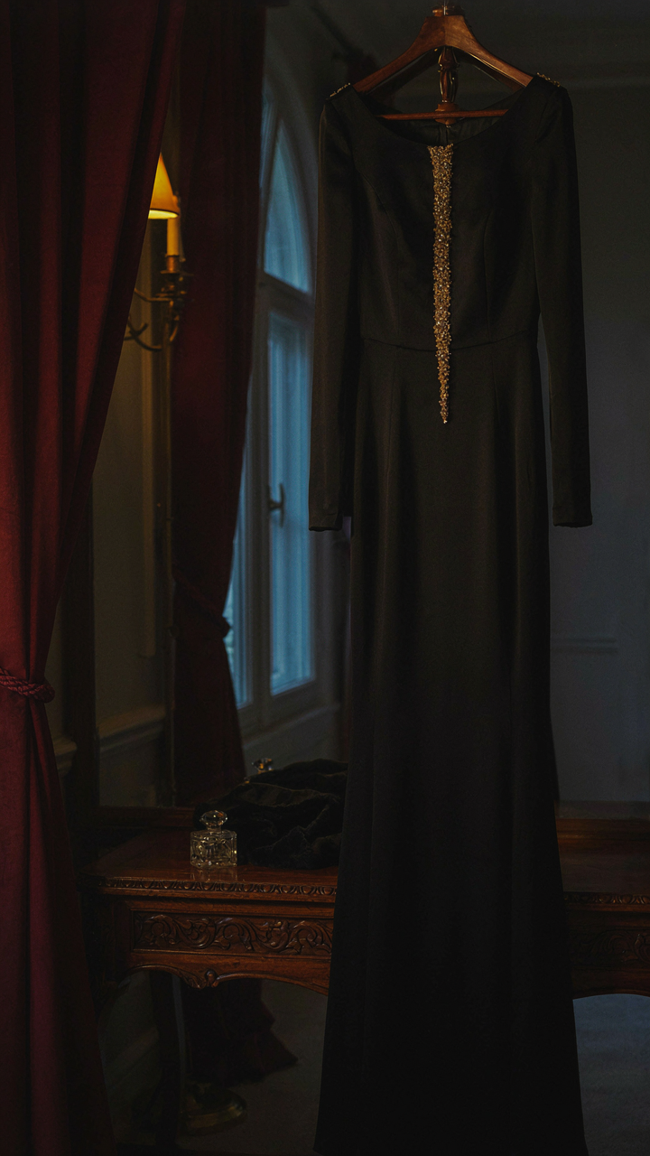 An elegant black gown with a single gold beaded panel in a luxurious room.