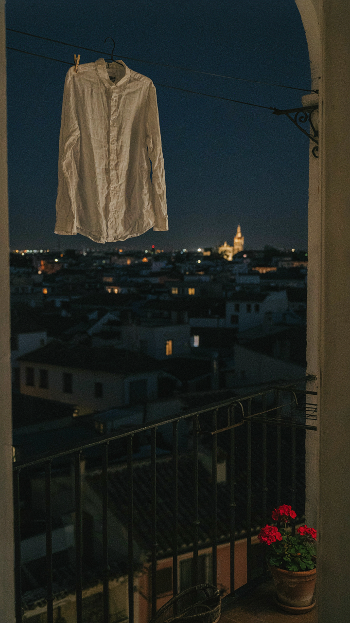 White linen shirt drying on a clothesline on a hotel balcony at night.