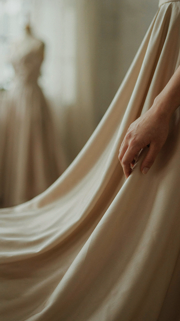 A hand gently touches luxurious, flowing silk charmeuse fabric, catching the light.