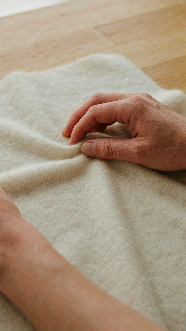A hand touches soft merino wool fabric, highlighting its quality.