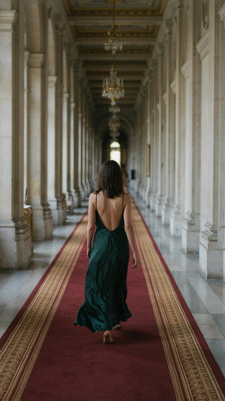 Woman walking away in a backless maxi dress in a grand hallway.