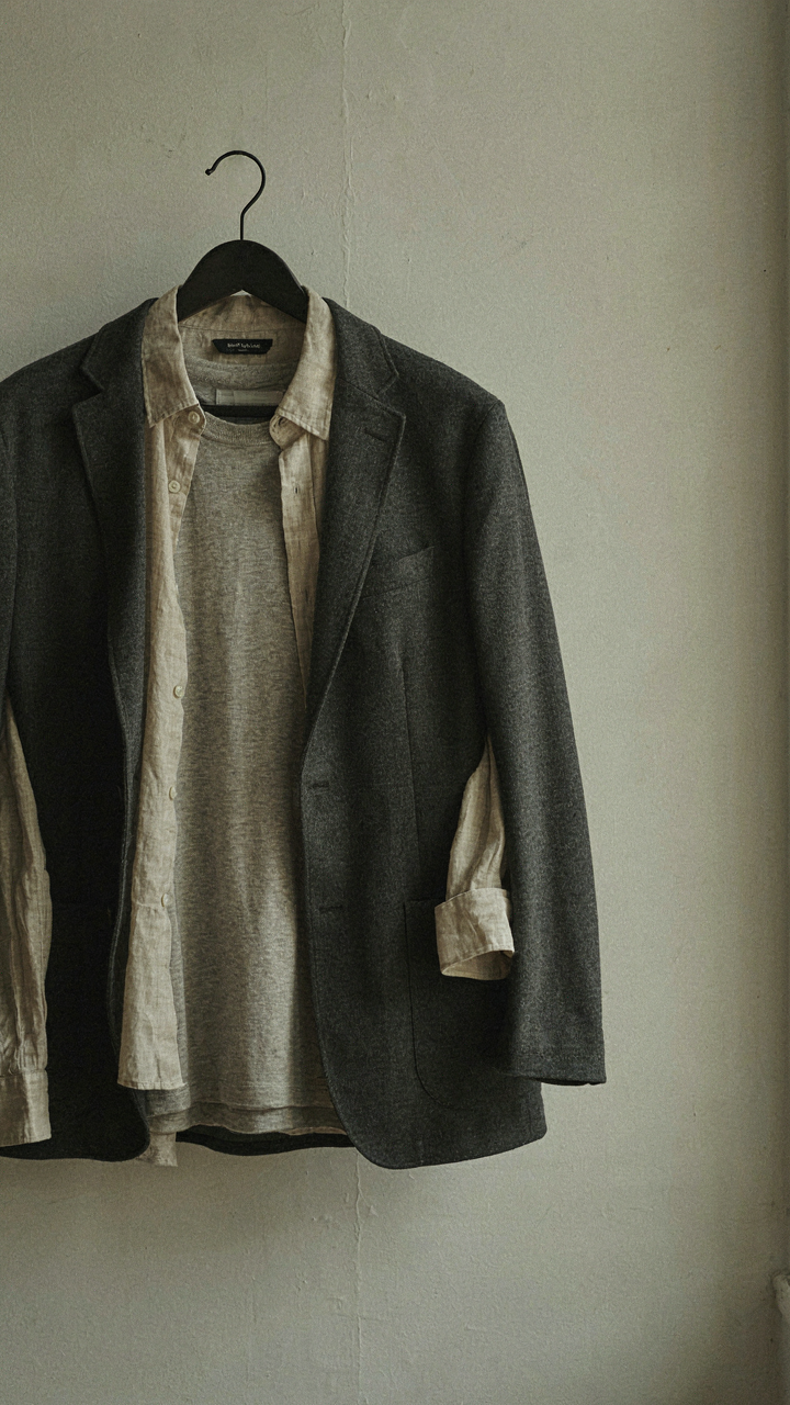 A layered outfit with merino, linen, and a blazer hangs on a hanger.