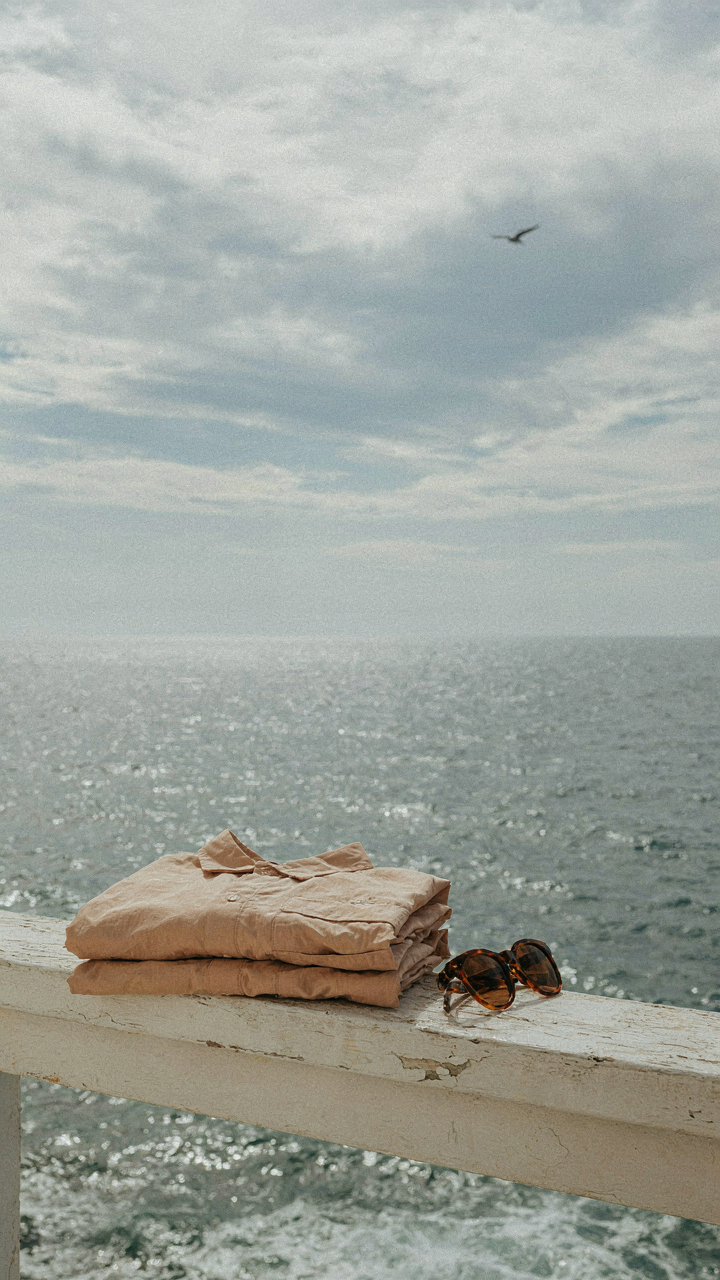 A folded quick-dry nylon overshirt rests on a railing by a cloudy sea.